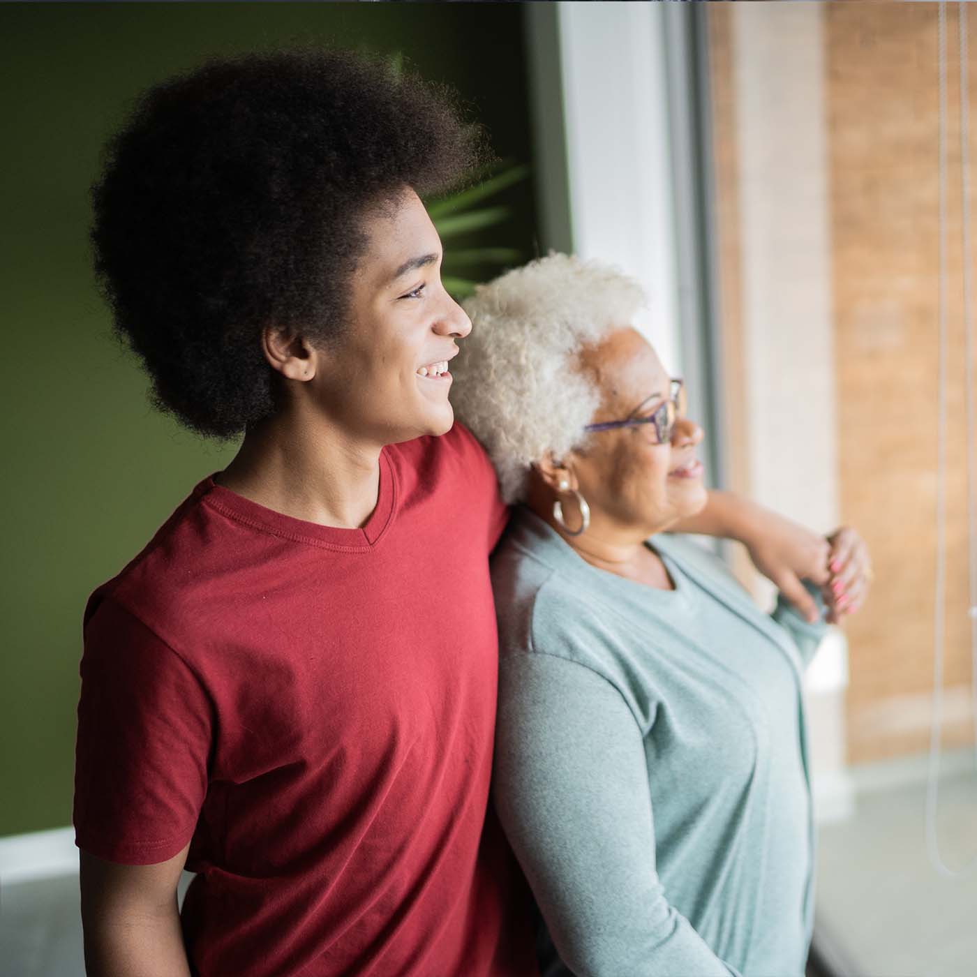 teenage boy standing with his grandma looking out a window of their home