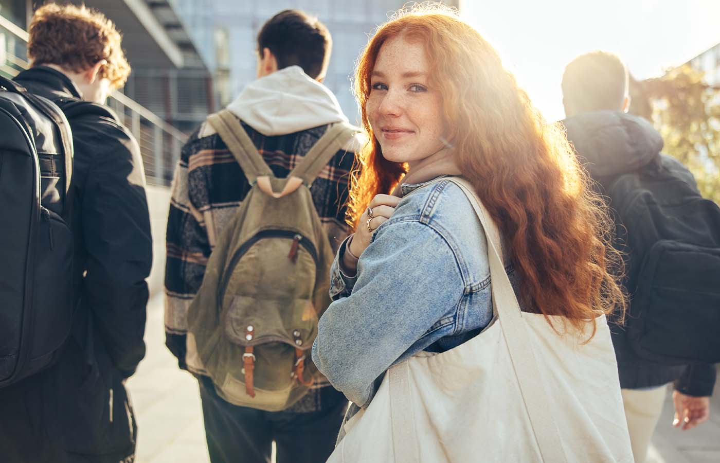 high school girl with red hair looking over her shoulder while walking toward class with a backpack on her shoulder